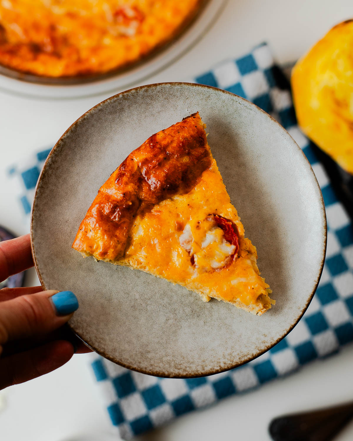 Hand holding a slice of spaghetti squash crustless quiche showing creamy texture and golden crust