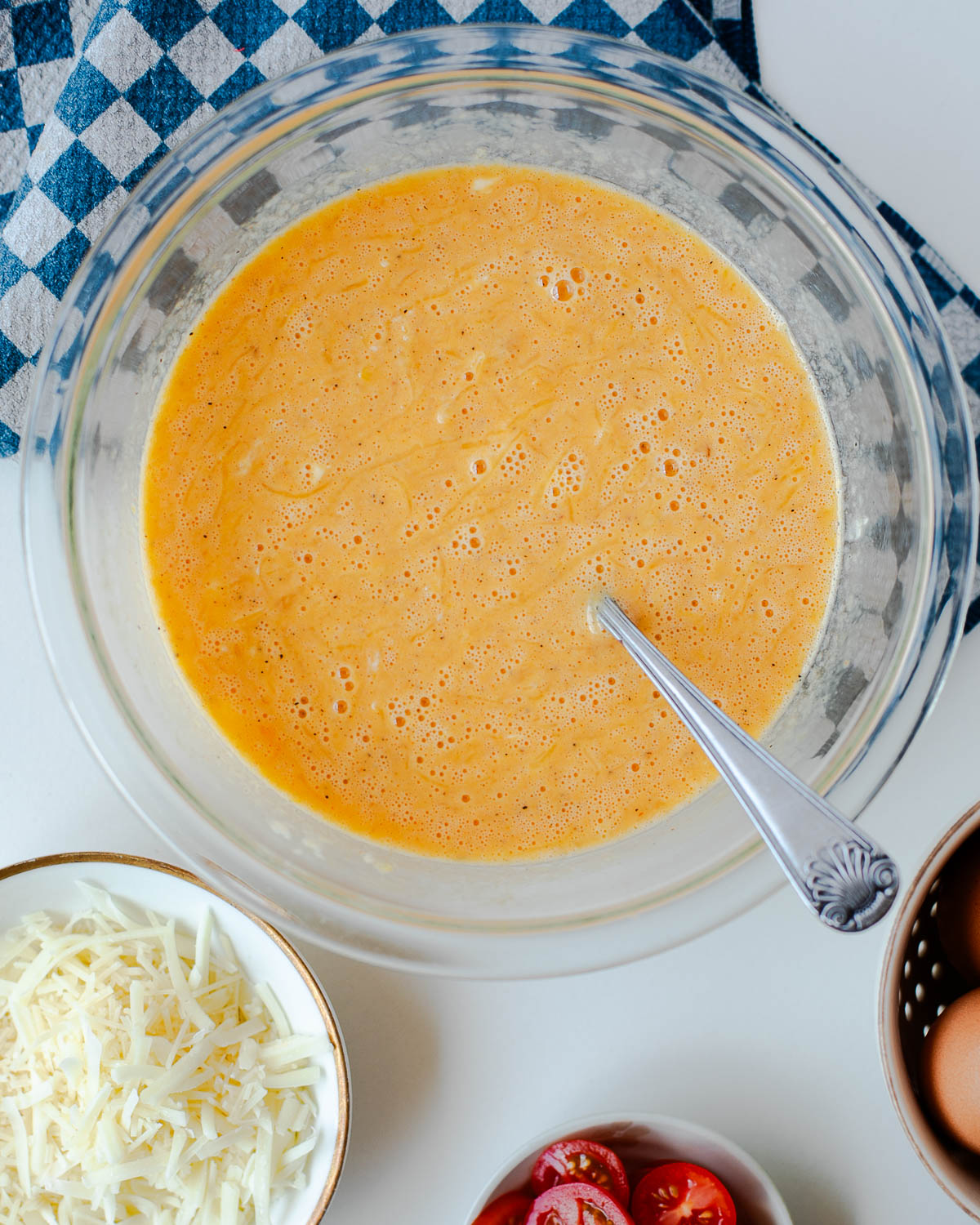 Whisked egg mixture with spaghetti squash and seasonings in a glass bowl for crustless quiche
