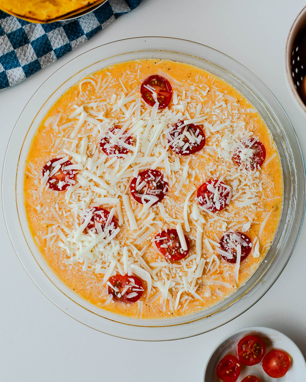 Unbaked spaghetti squash crustless quiche topped with shredded mozzarella and sliced grape tomatoes