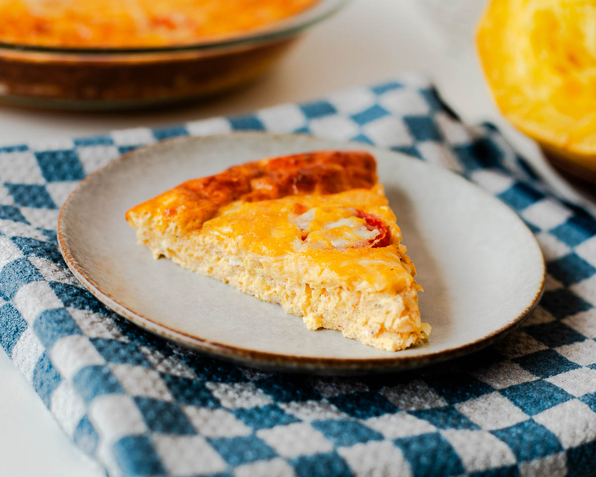 High protein spaghetti squash quiche slice on a plate with fluffy egg texture and tomatoes
