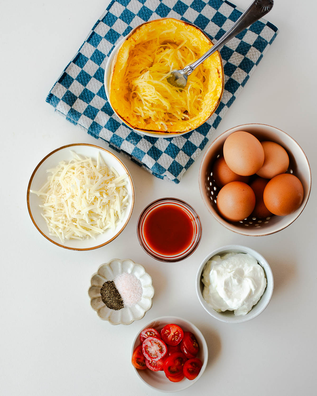 Ingredients for spaghetti squash crustless quiche including eggs, yogurt, cheese, tomatoes, and squash