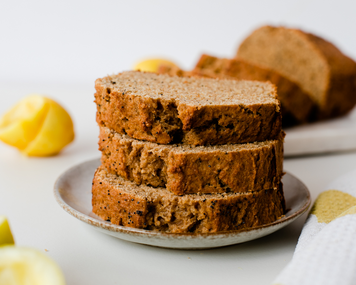 Plate of lemon poppy seed bread slices; full loaf and lemons in background