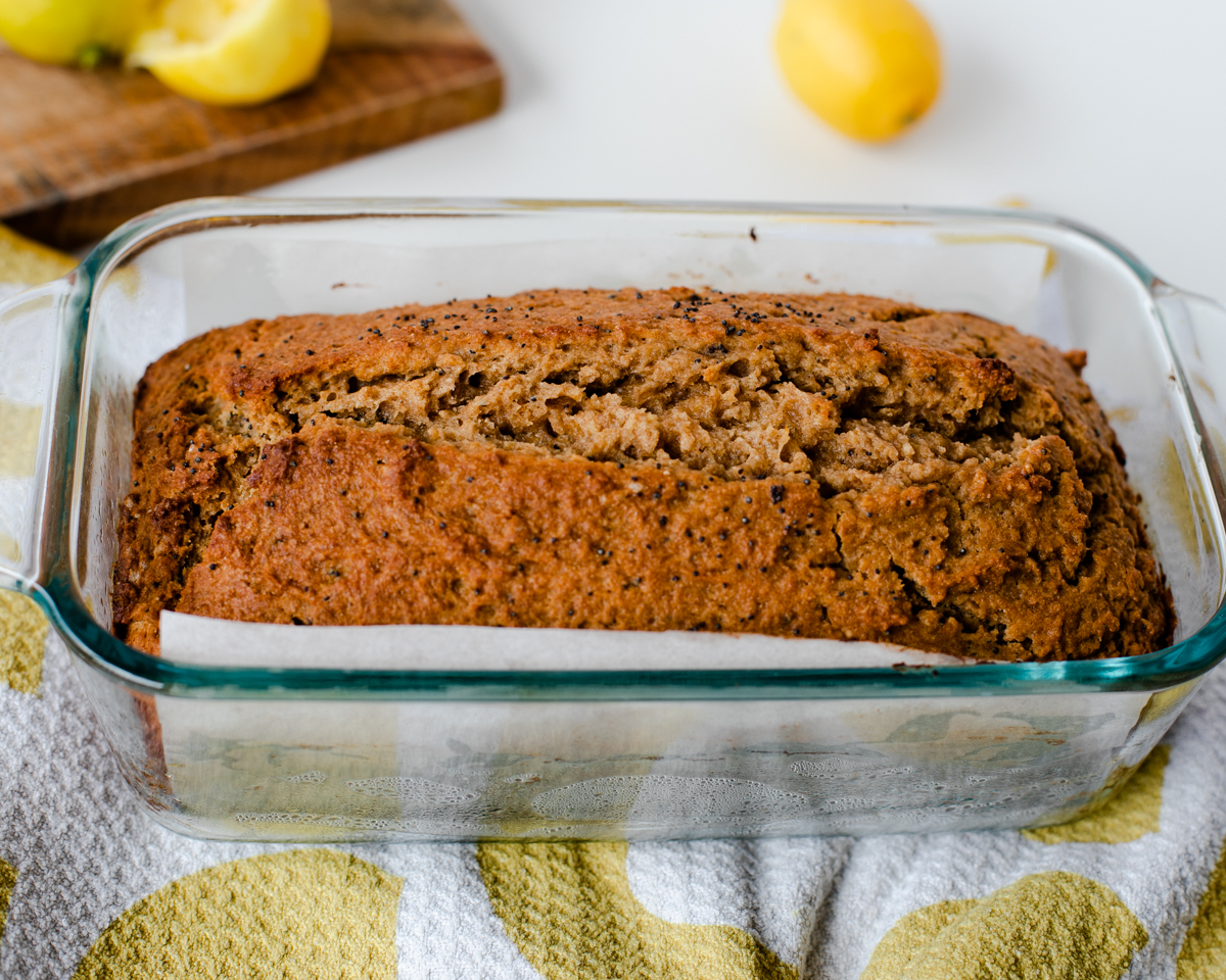 Golden whole wheat lemon poppy seed bread resting in pan with parchment lining