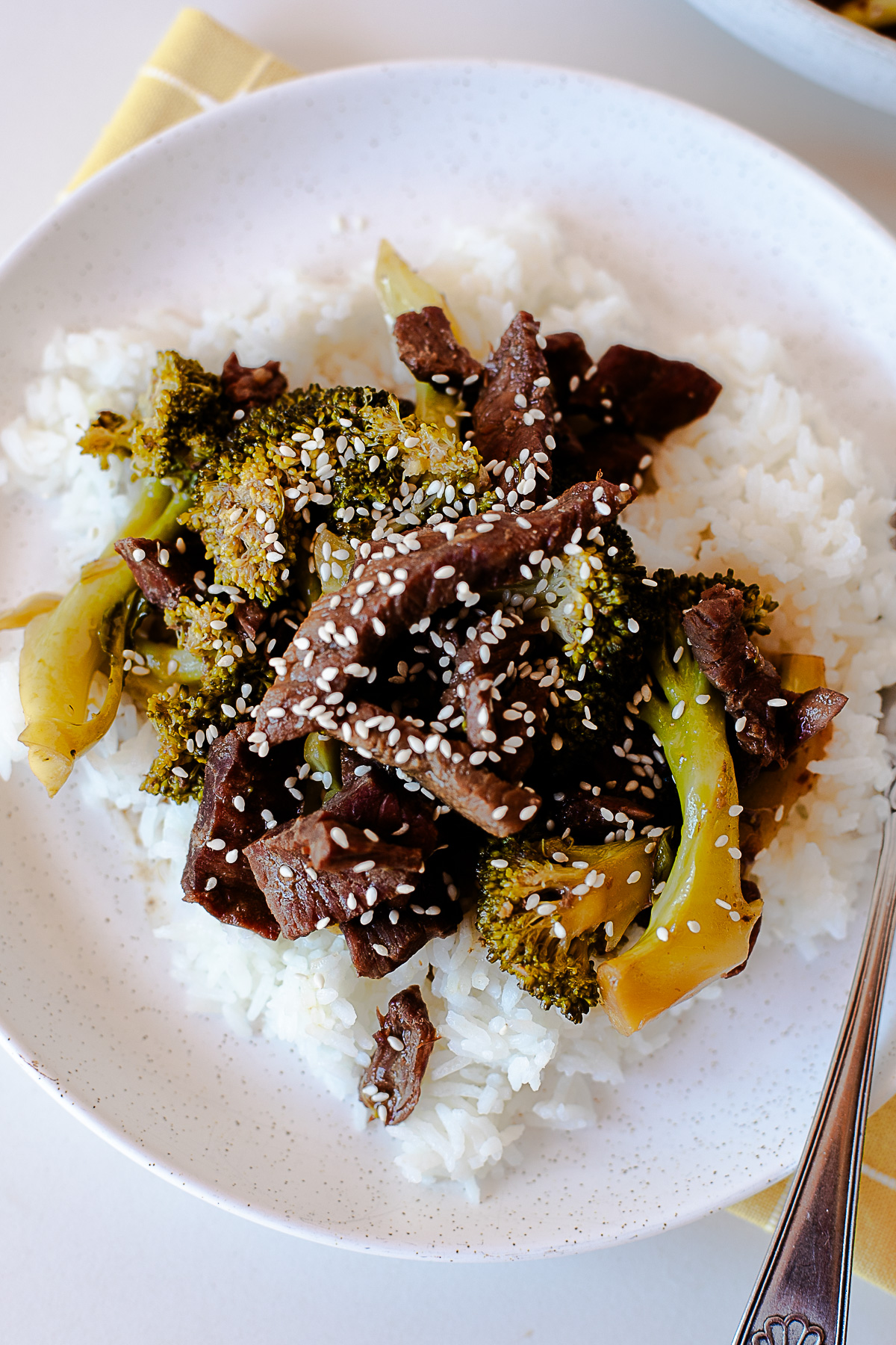 Overhead shot of a plate of beef and broccoli over white rice, topped with sesame seeds.
