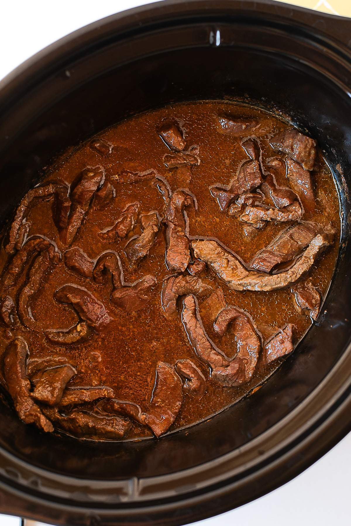 Close-up of cooked beef in a rich brown sauce inside the crockpot.
