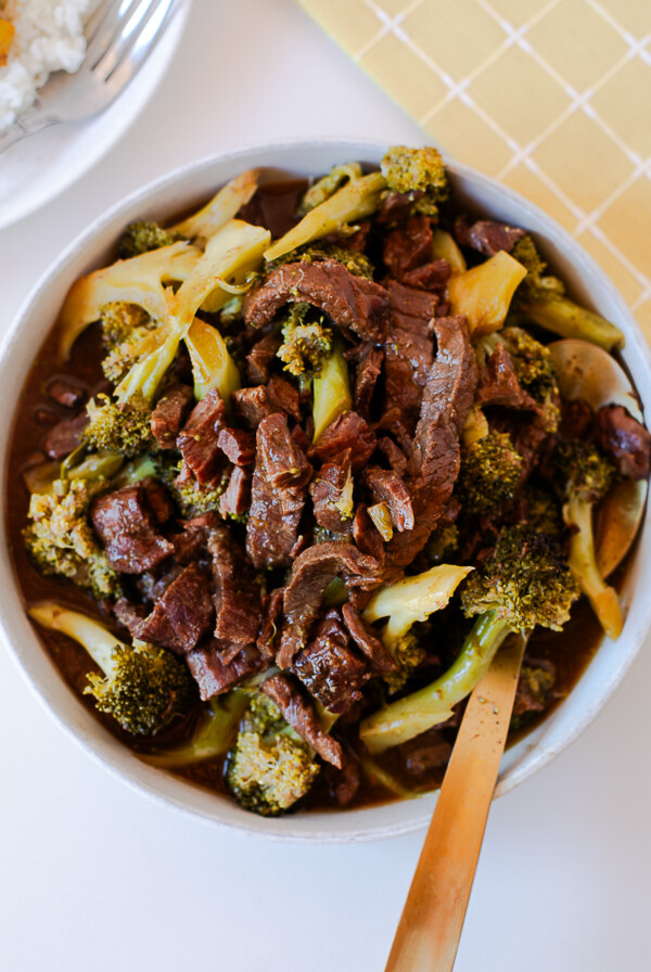 Overhead shot of a bowl of crockpot beef and broccoli with a spoon, rice visible in the background.