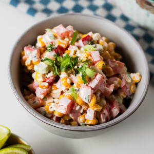 A bowl of creamy Mexican street corn salad made with sweet corn, red bell pepper, green onions, cotija cheese, and a tangy lime dressing.