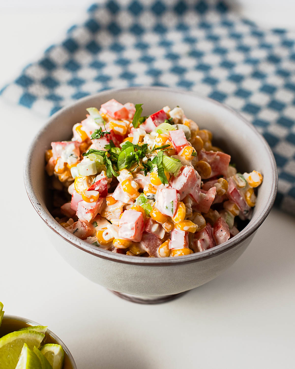 A bowl of creamy Mexican street corn salad made with sweet corn, red bell pepper, green onions, cotija cheese, and a tangy lime dressing.