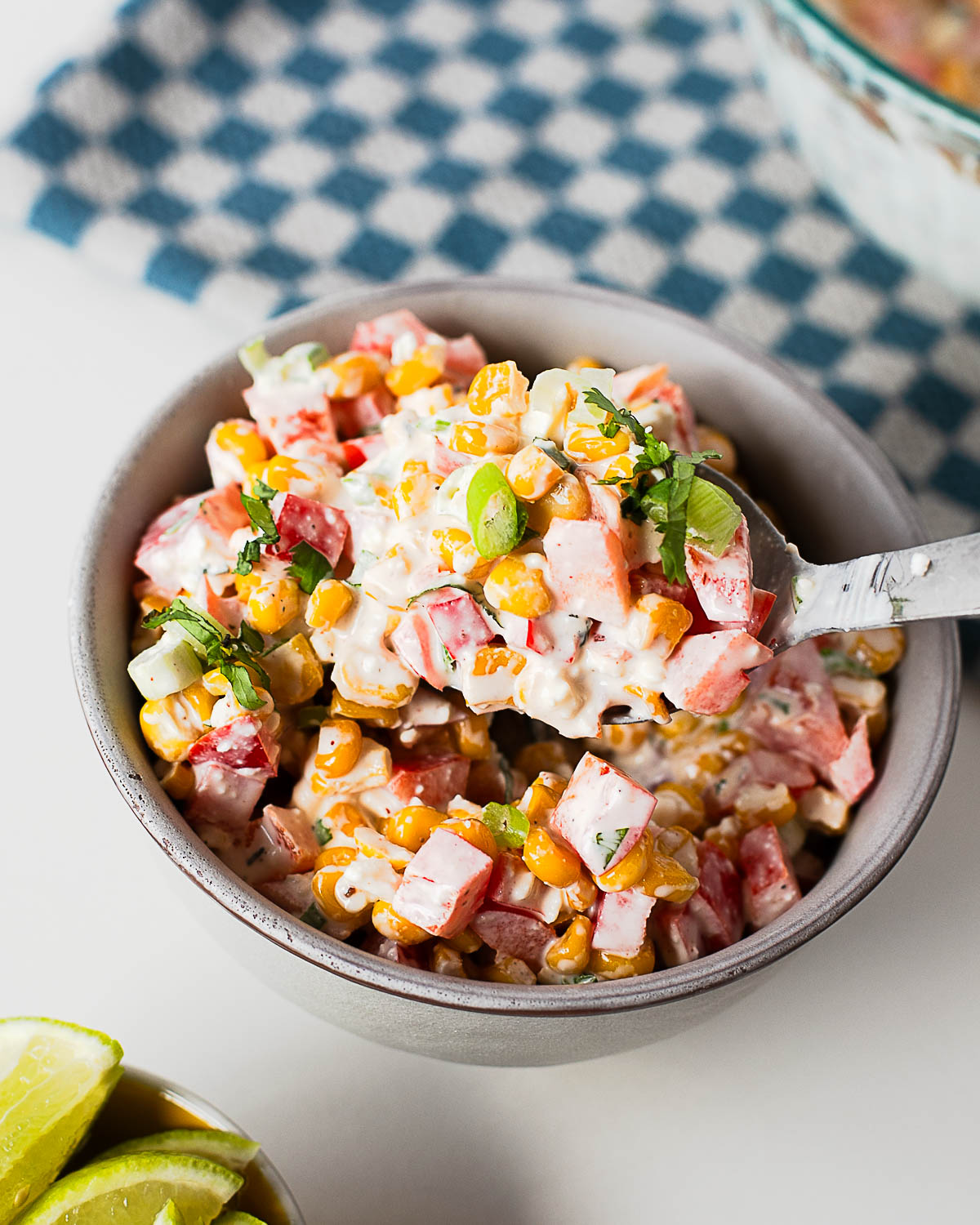 Spoonful of creamy Mexican street corn salad showing sweet corn kernels, red bell pepper, fresh herbs, and flavorful dressing.