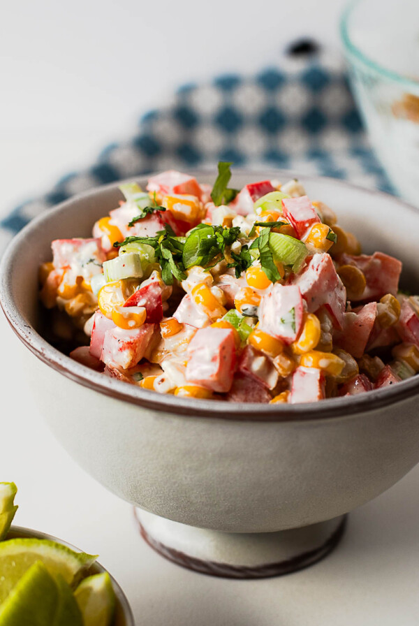 Easy Mexican street corn salad served in a bowl with fresh lime wedges, featuring sweet corn, cotija cheese, bell pepper, and creamy dressing.