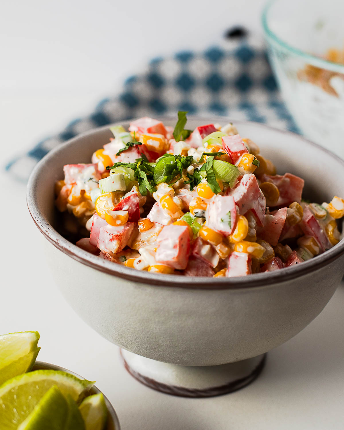 Easy Mexican street corn salad served in a bowl with fresh lime wedges, featuring sweet corn, cotija cheese, bell pepper, and creamy dressing.
