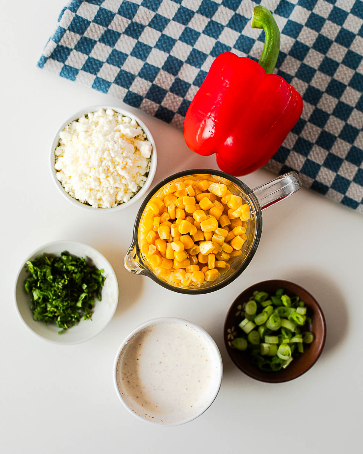 Ingredients for Mexican street corn salad including corn kernels, cotija cheese, red bell pepper, green onions, cilantro, and creamy chili lime dressing.