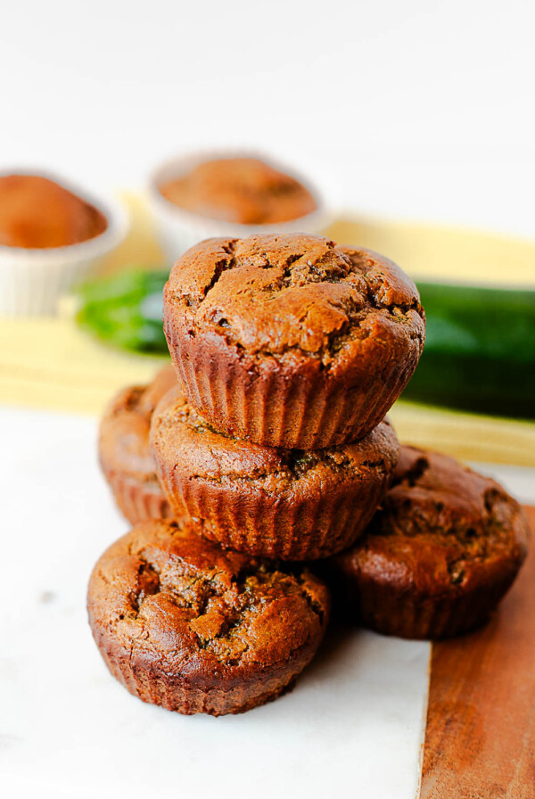 Tall stack of almond butter zucchini muffins with a fresh zucchini in the background
