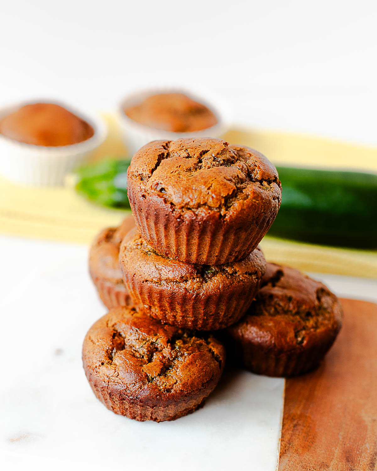 Tall stack of almond butter zucchini muffins with a fresh zucchini in the background
