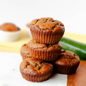 Almond butter zucchini muffins piled on a serving board with fresh zucchini behind them
