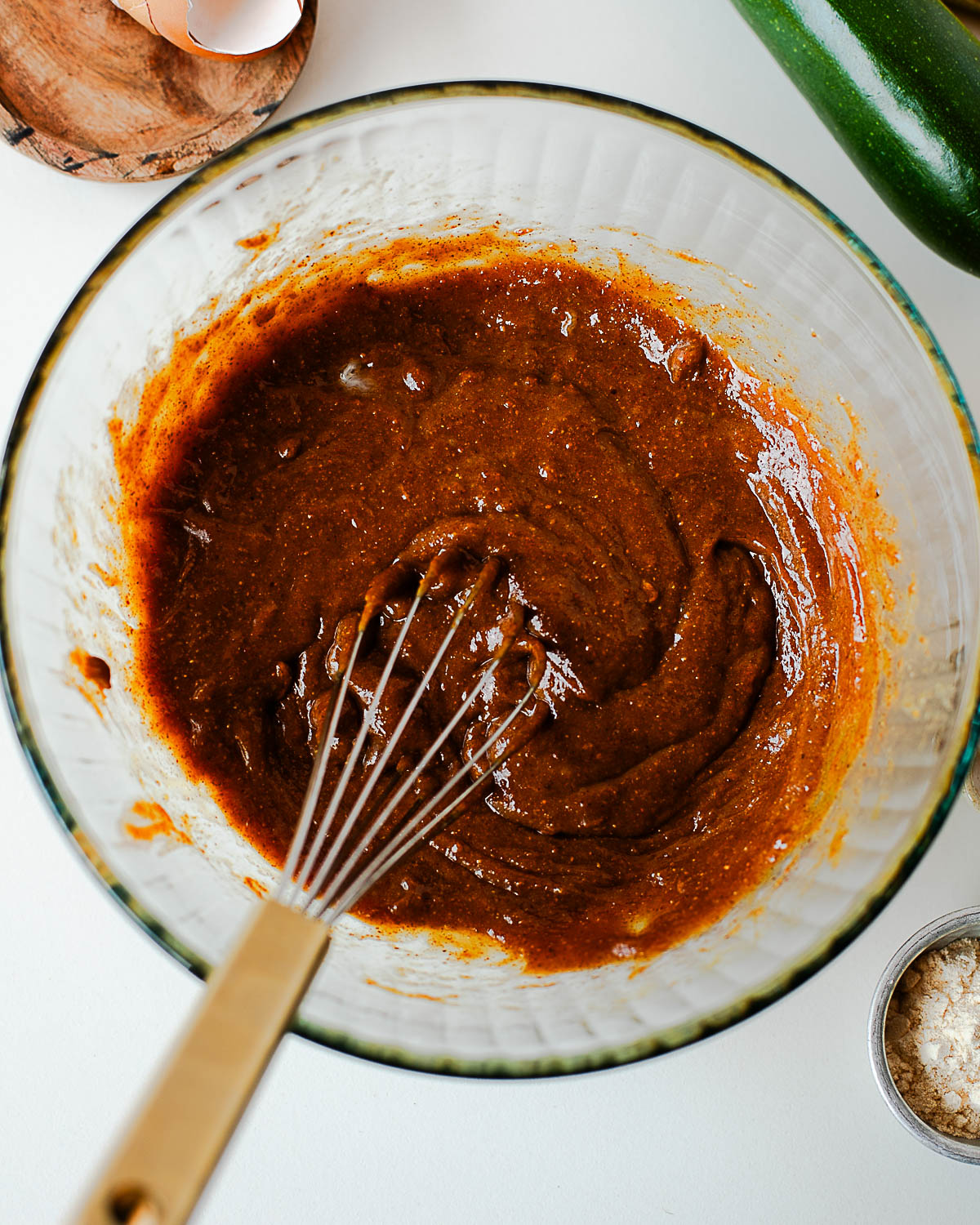 Batter being whisked in a glass bowl with a fresh zucchini nearby