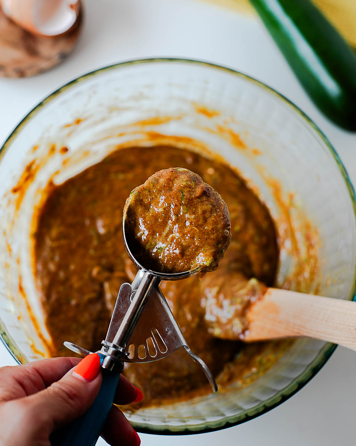 Cookie scoop lifting a portion of almond butter zucchini muffin batter from the bowl