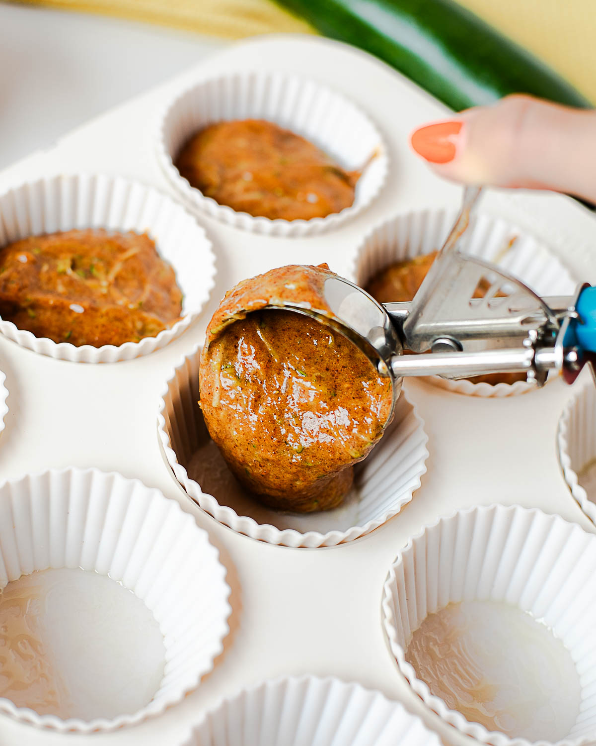 Cookie scoop lifting a portion of zucchini muffin batter from the bowl