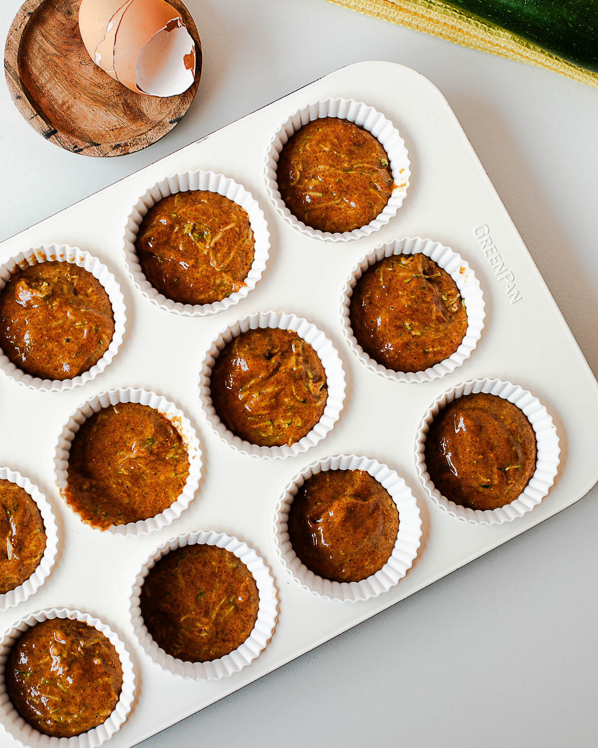 Unbaked almond butter zucchini muffins in a white muffin tin ready for the oven