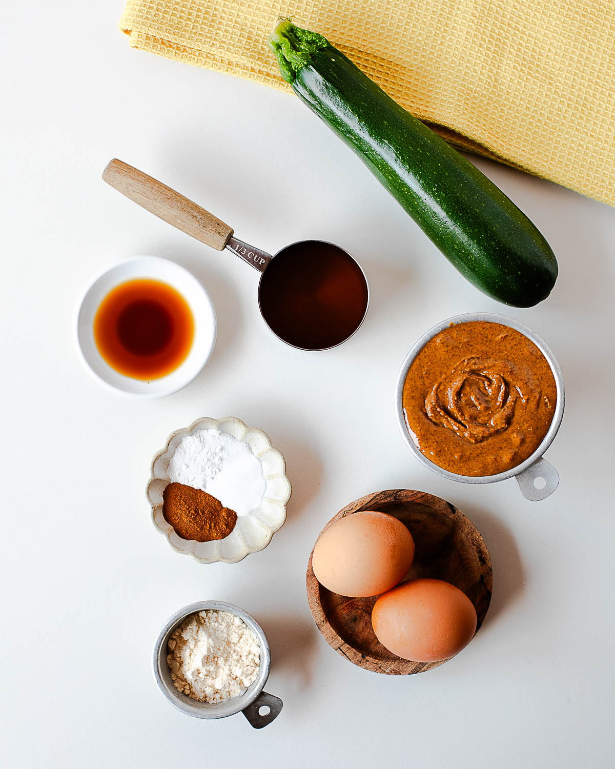 Ingredients for gluten free zucchini muffins including eggs, almond butter, honey, coconut flour, vanilla, spices, and zucchini