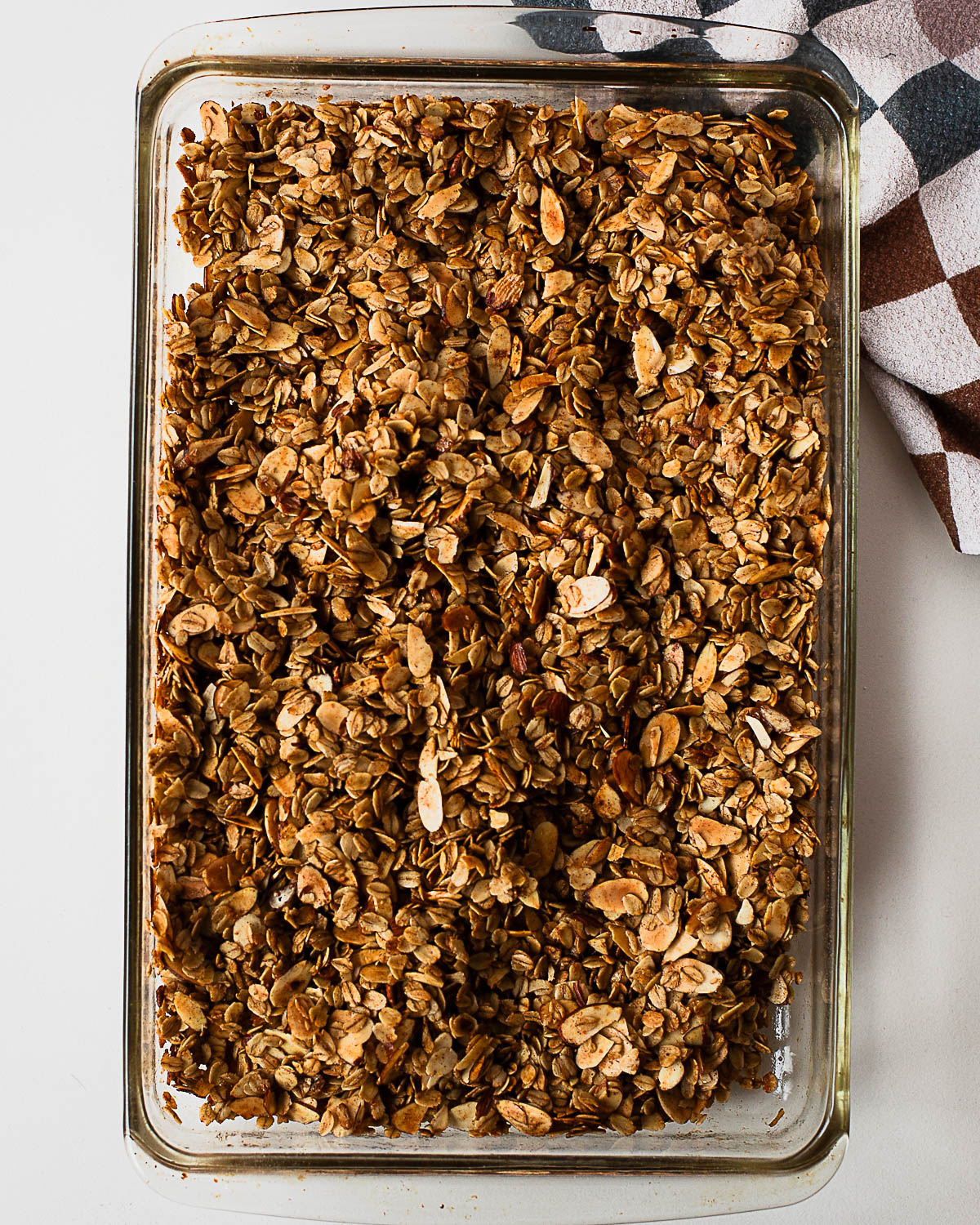 Golden-brown baked olive oil granola in a glass baking dish, perfectly toasted and crisp after baking.