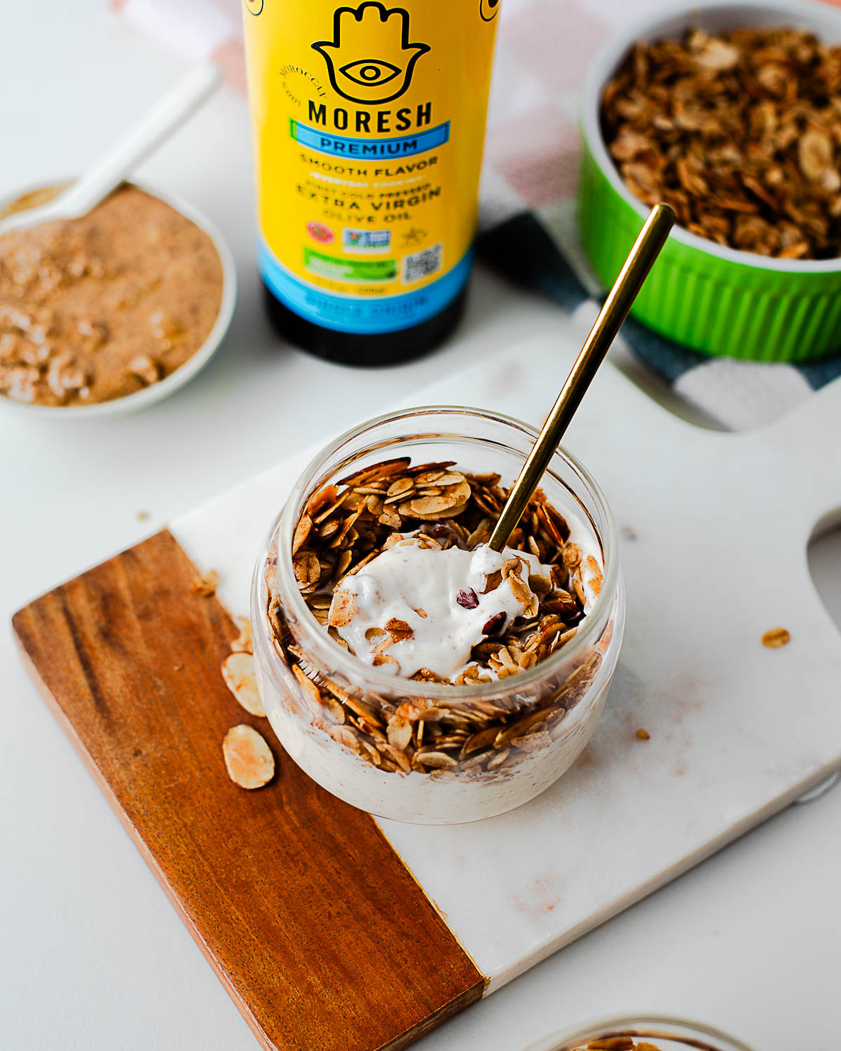 Jar of yogurt topped with almond maple olive oil granola and a gold spoon — creamy and crunchy layers ready to eat.