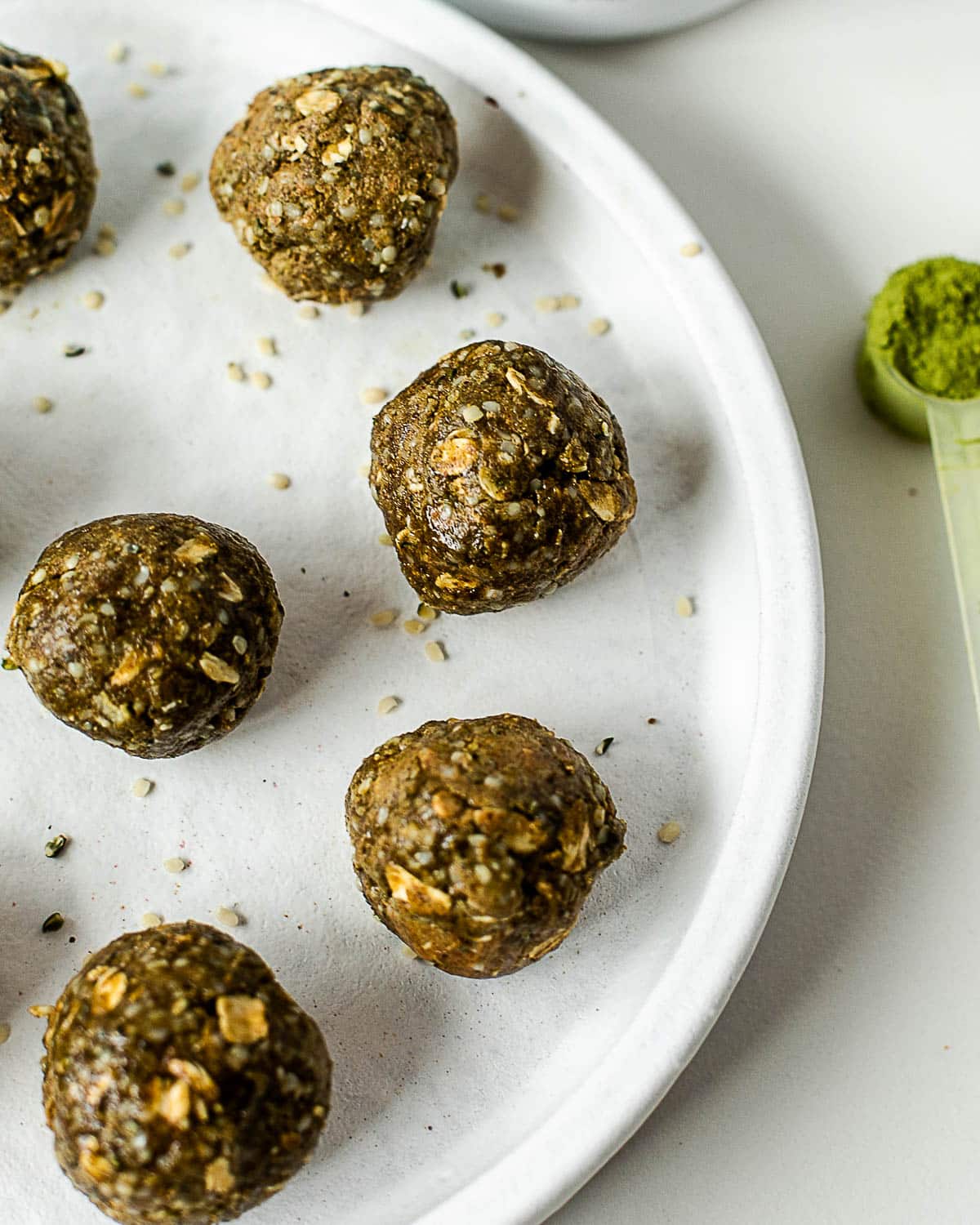Homemade matcha energy bites with a soft chewy texture served on a white plate with matcha powder nearby.