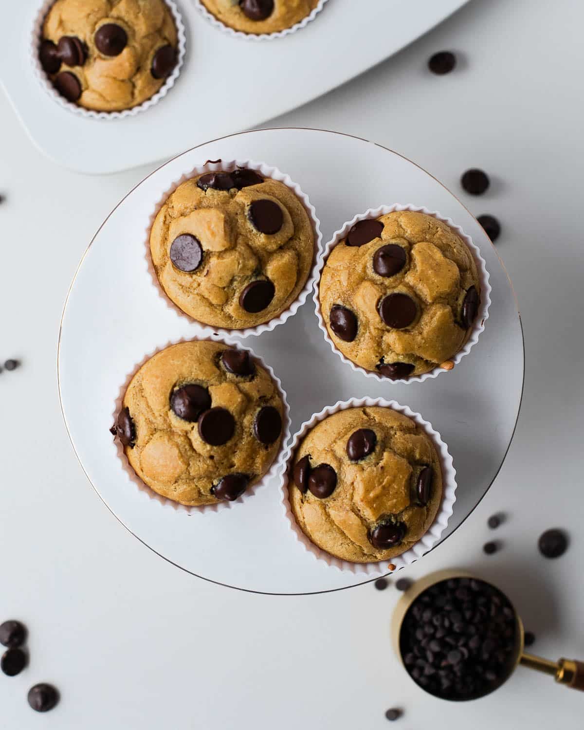 Healthy chocolate chip chickpea muffins arranged on a baking tray with dark chocolate chips scattered nearby.