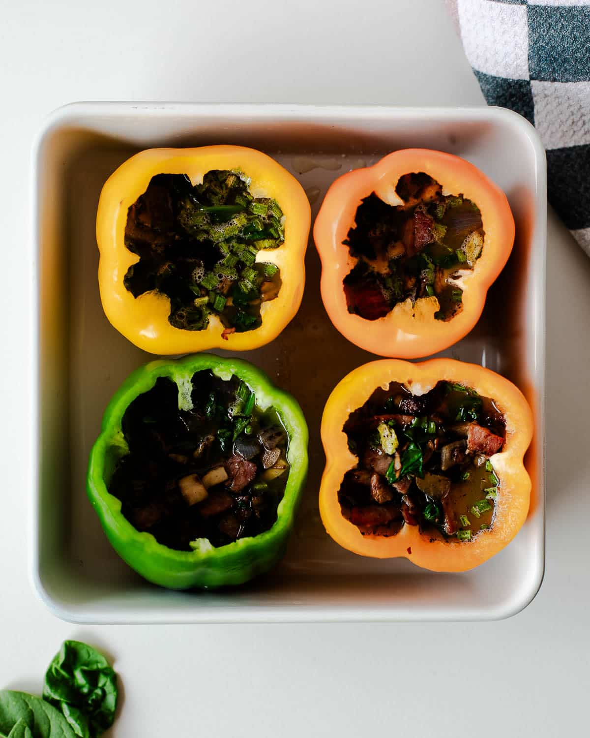 Raw egg stuffed peppers in a pan, filled with veggies and egg mixture.