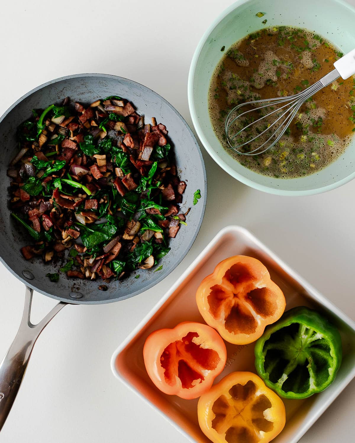 Skillet of turkey bacon, mushrooms, spinach; whisked eggs and hollow bell peppers ready to fill.