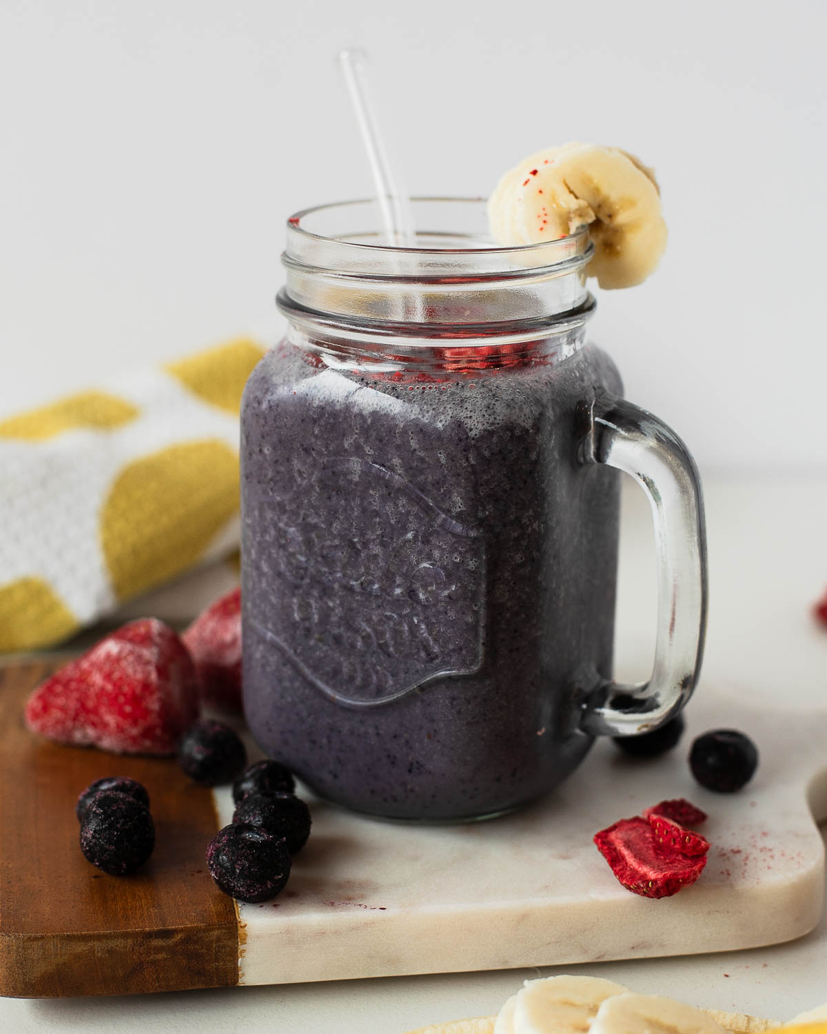 Mason jar of blueberry-strawberry egg white protein shake with banana garnish and glass straw.