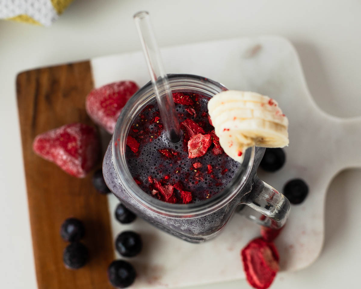 Close-up of frothy berry egg white smoothie with strawberry bits and banana garnish.