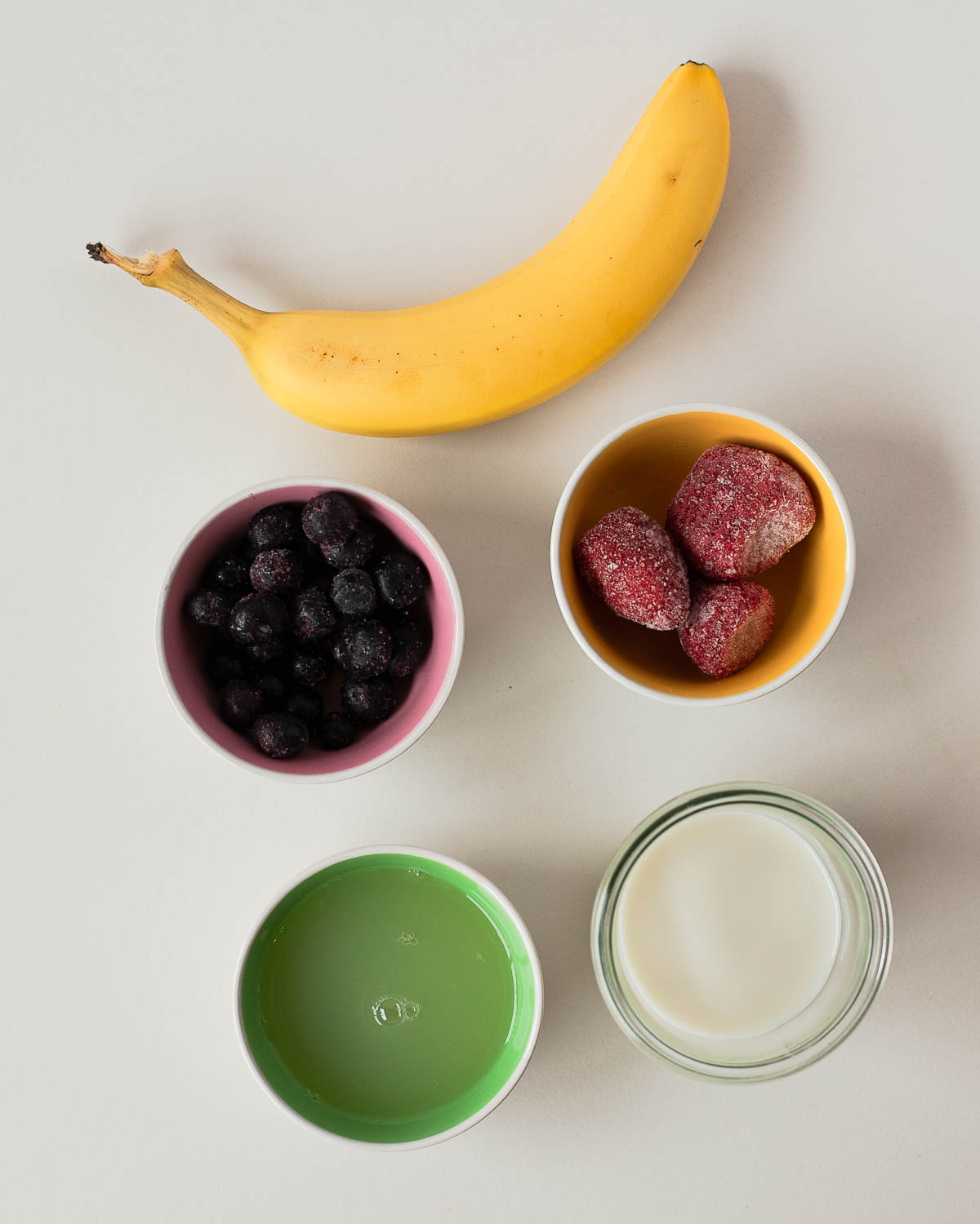 Ingredients flat lay for egg white protein shake—banana, frozen strawberries and blueberries, liquid egg whites, and almond milk.