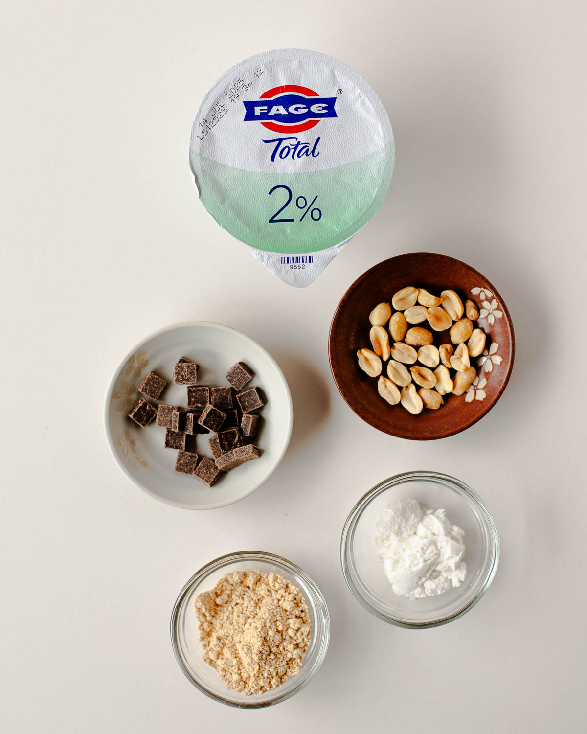 Ingredients for Snickers yogurt cups—Greek yogurt, dark chocolate, peanuts, peanut powder and vanilla protein powder.