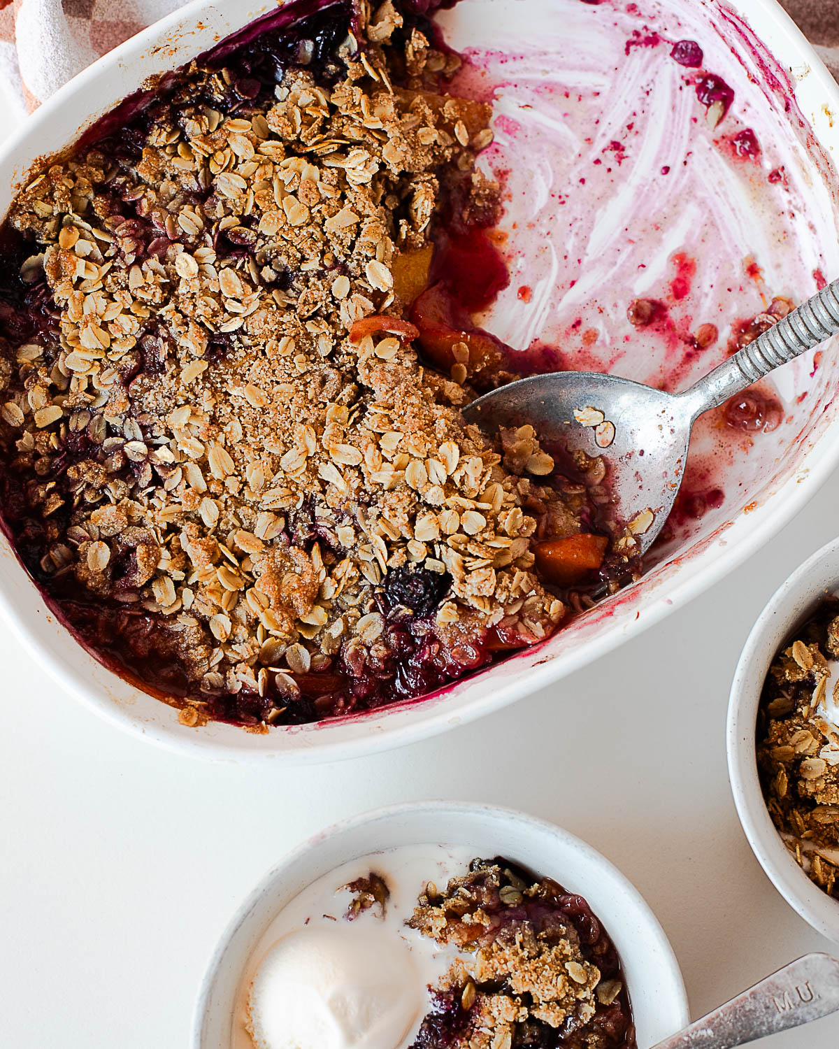 Overhead of half-eaten blueberry peach crisp and two bowls ready to serve.
