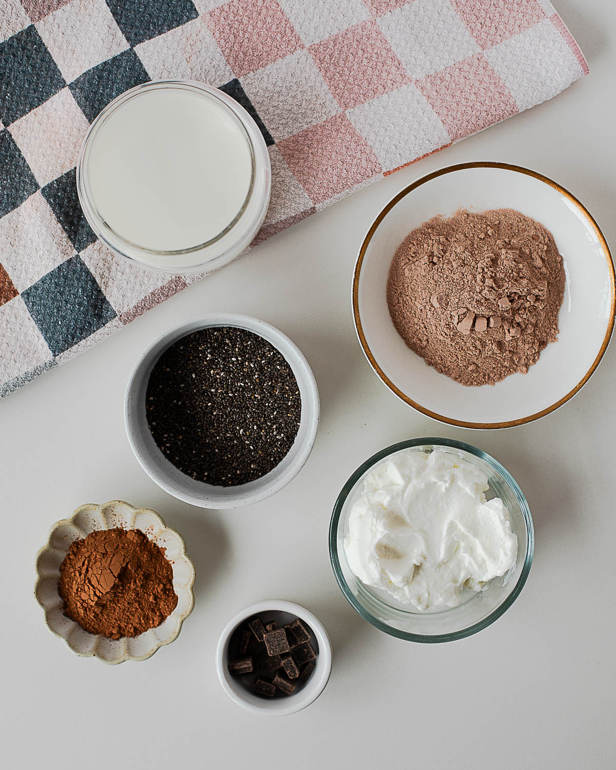 Overhead of ingredients for chocolate protein chia pudding: milk, yogurt, chia, cocoa, protein powder, dark chocolate.