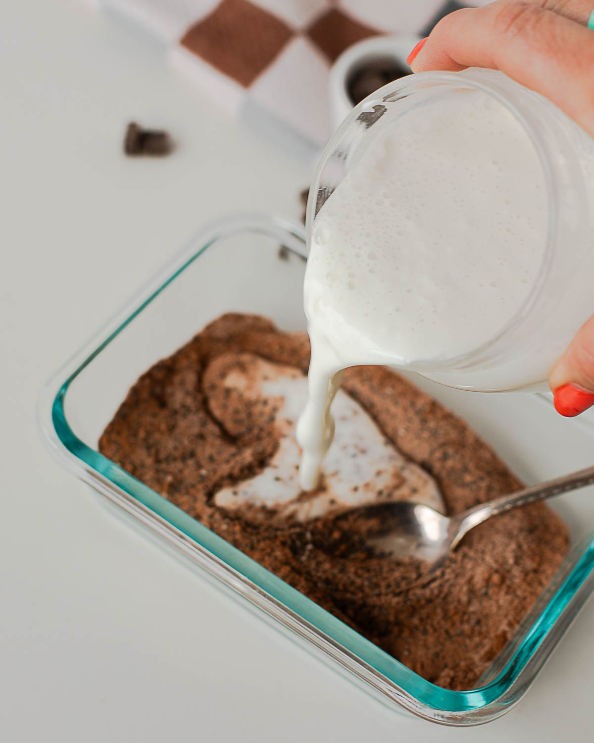 Pouring almond milk into chia, cocoa, and protein powder to start chocolate protein chia pudding.