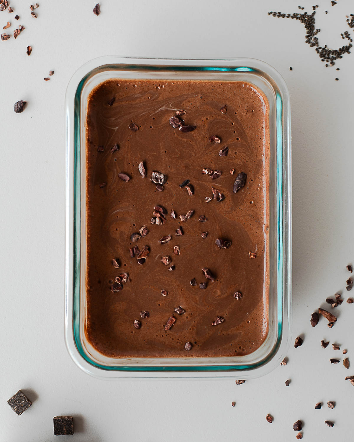 Chocolate chia pudding in a glass container topped with cacao nibs before chilling.