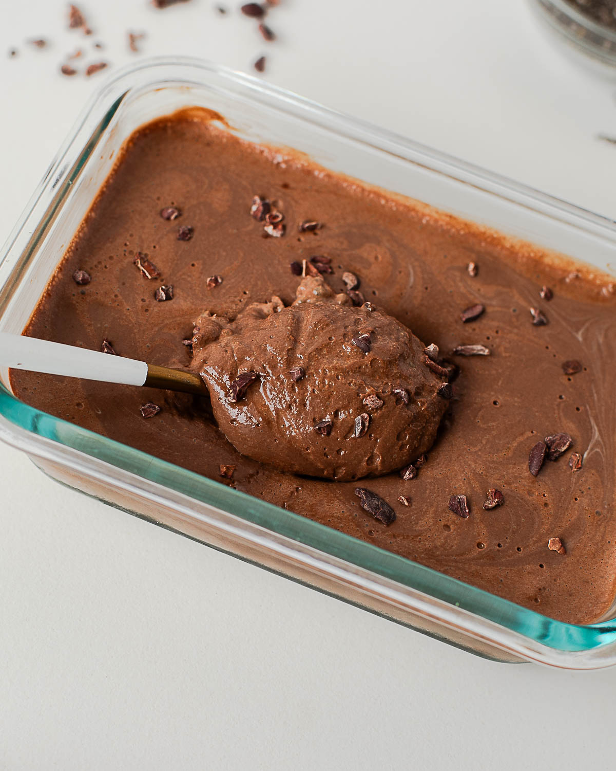 Set creamy chocolate chia pudding with cacao nibs, spoon resting on top.