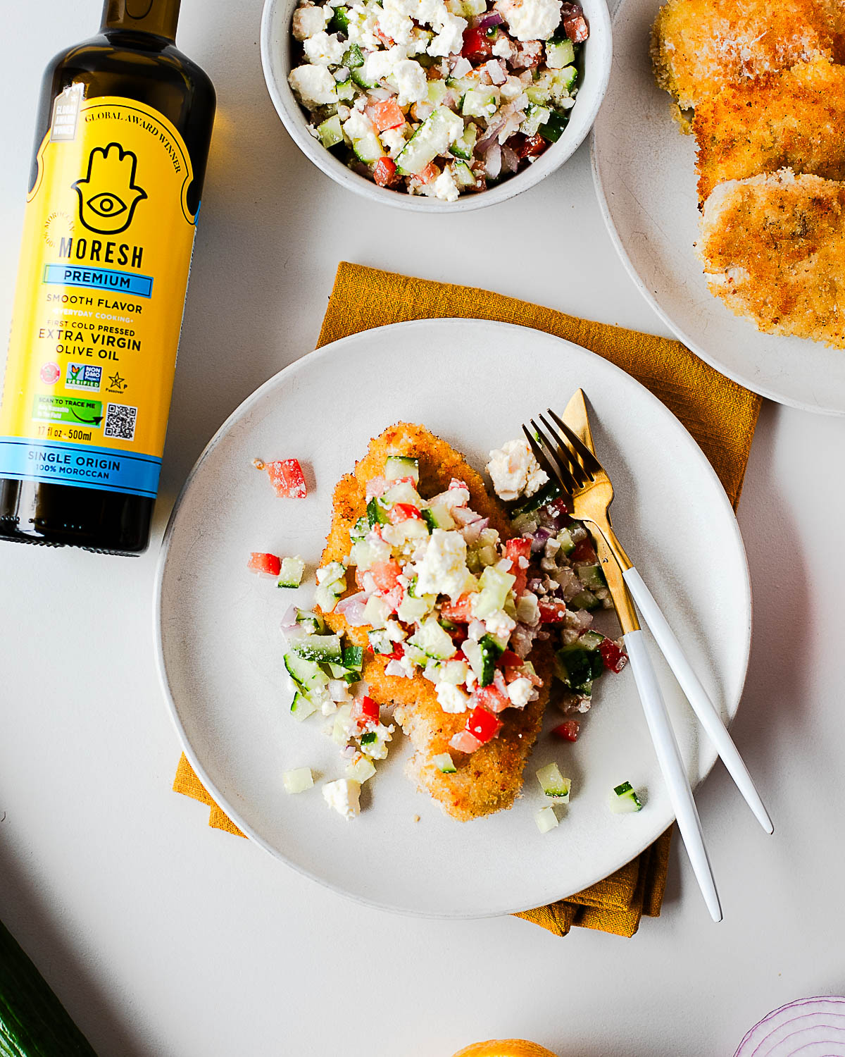 Table scene with plated cutlets, Mediterranean salad, and Moresh olive oil.