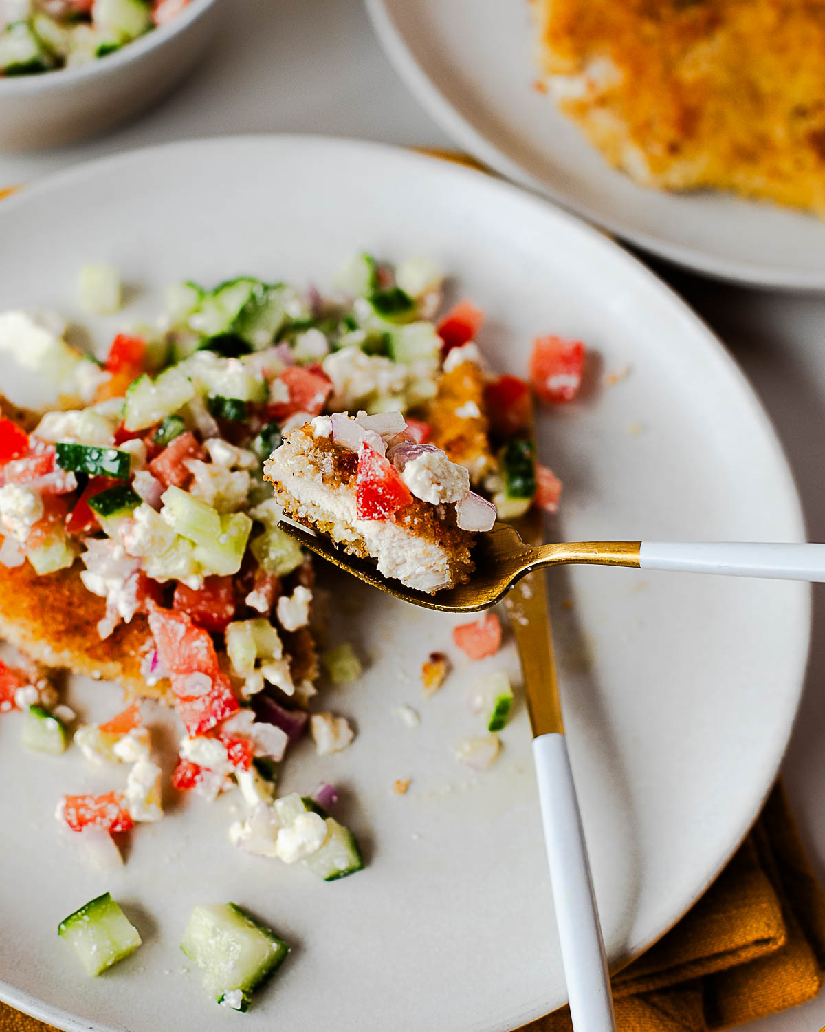 Fork lifting a bite of crispy chicken cutlet with cucumber-feta salad.