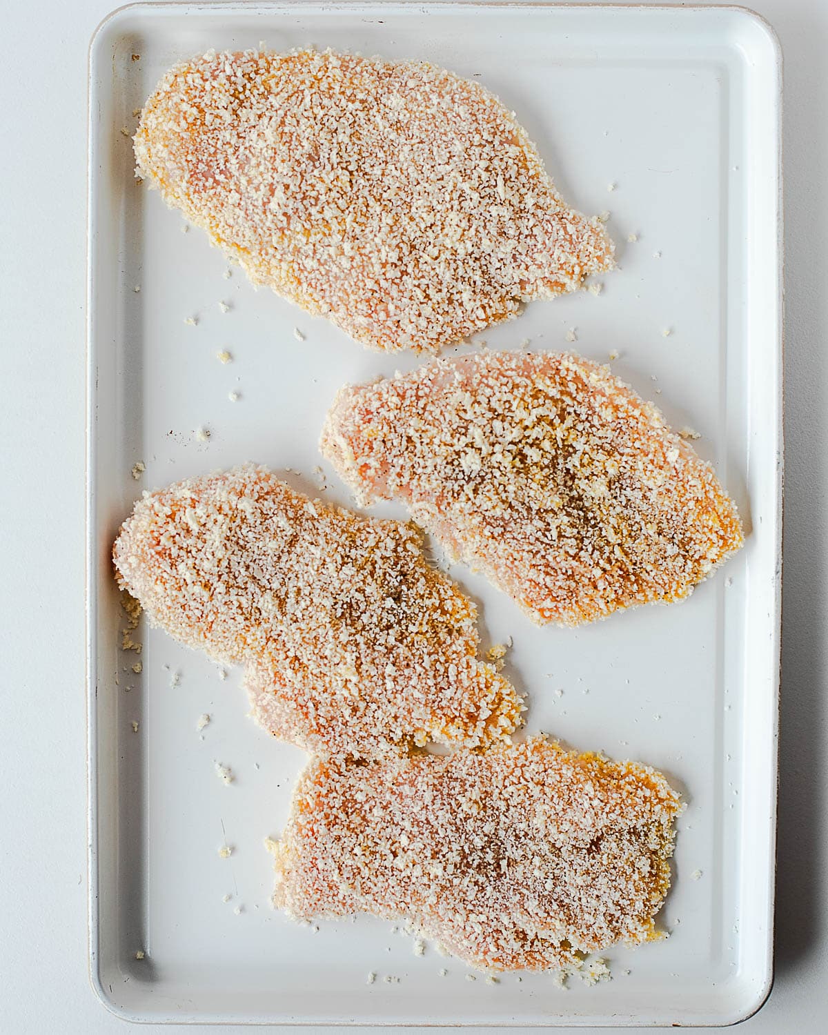 Breaded chicken cutlets on a sheet pan, ready to fry.