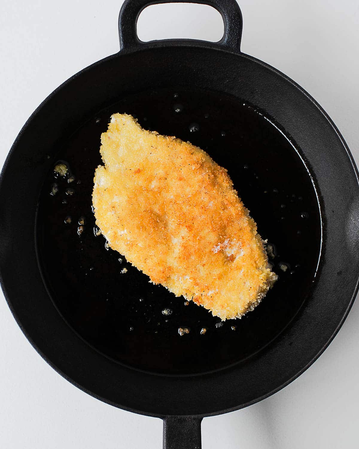 Chicken cutlet shallow-frying in a cast-iron skillet with olive oil.