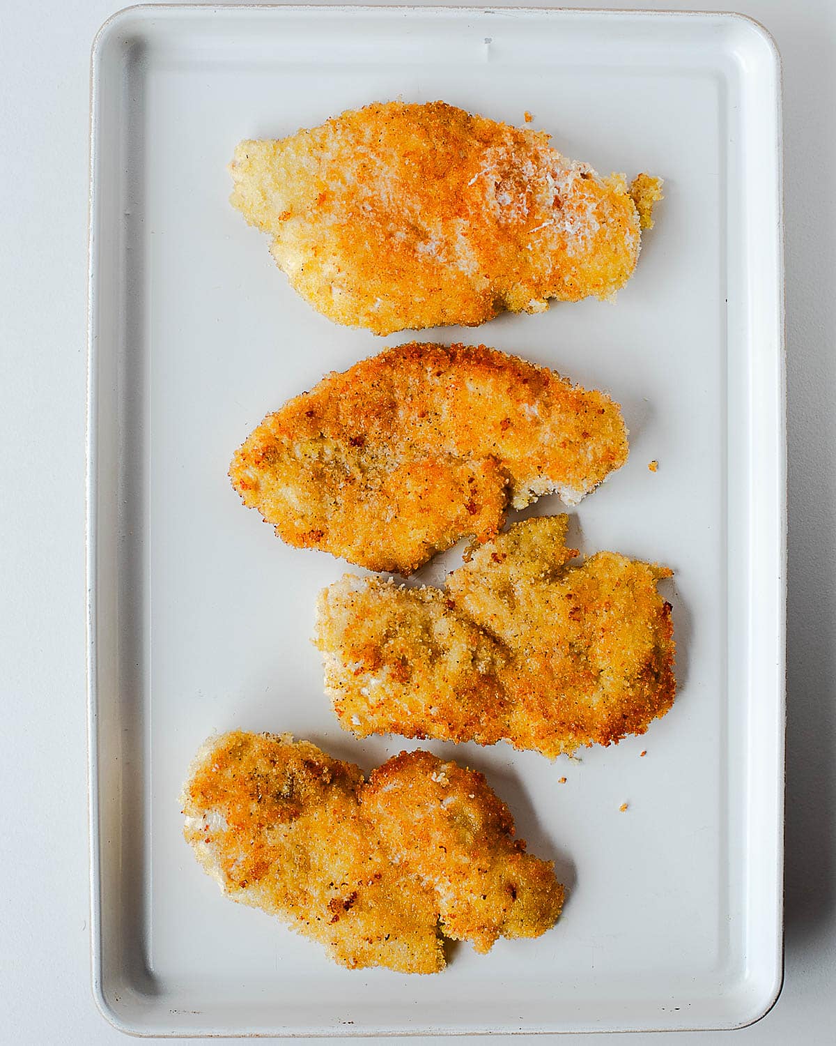 Golden brown chicken cutlets resting on a baking sheet after frying.