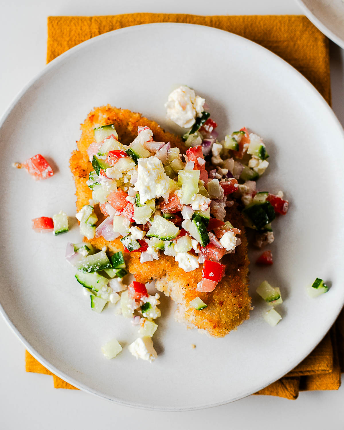 Close-up plate of crispy chicken cutlet with fresh Mediterranean topping.