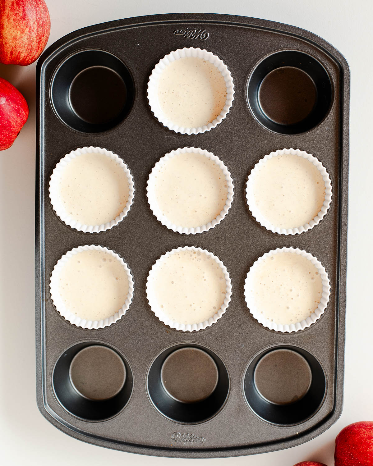Cheesecake batter poured into muffin liners in a muffin tin, ready to be baked into mini apple pie cheesecakes.