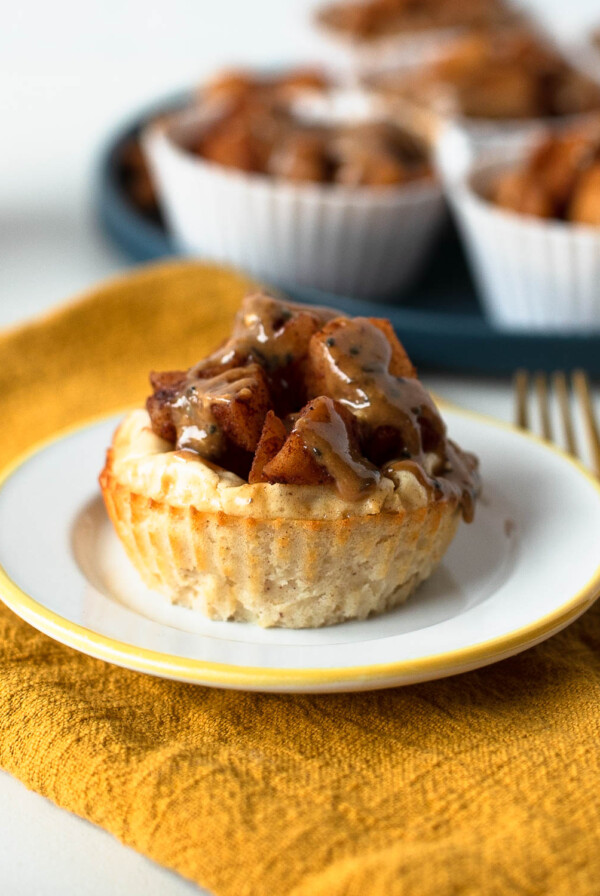 Close-up of a single mini apple pie cheesecake topped with warm cinnamon apples and almond butter drizzle on a yellow napkin with fork nearby.