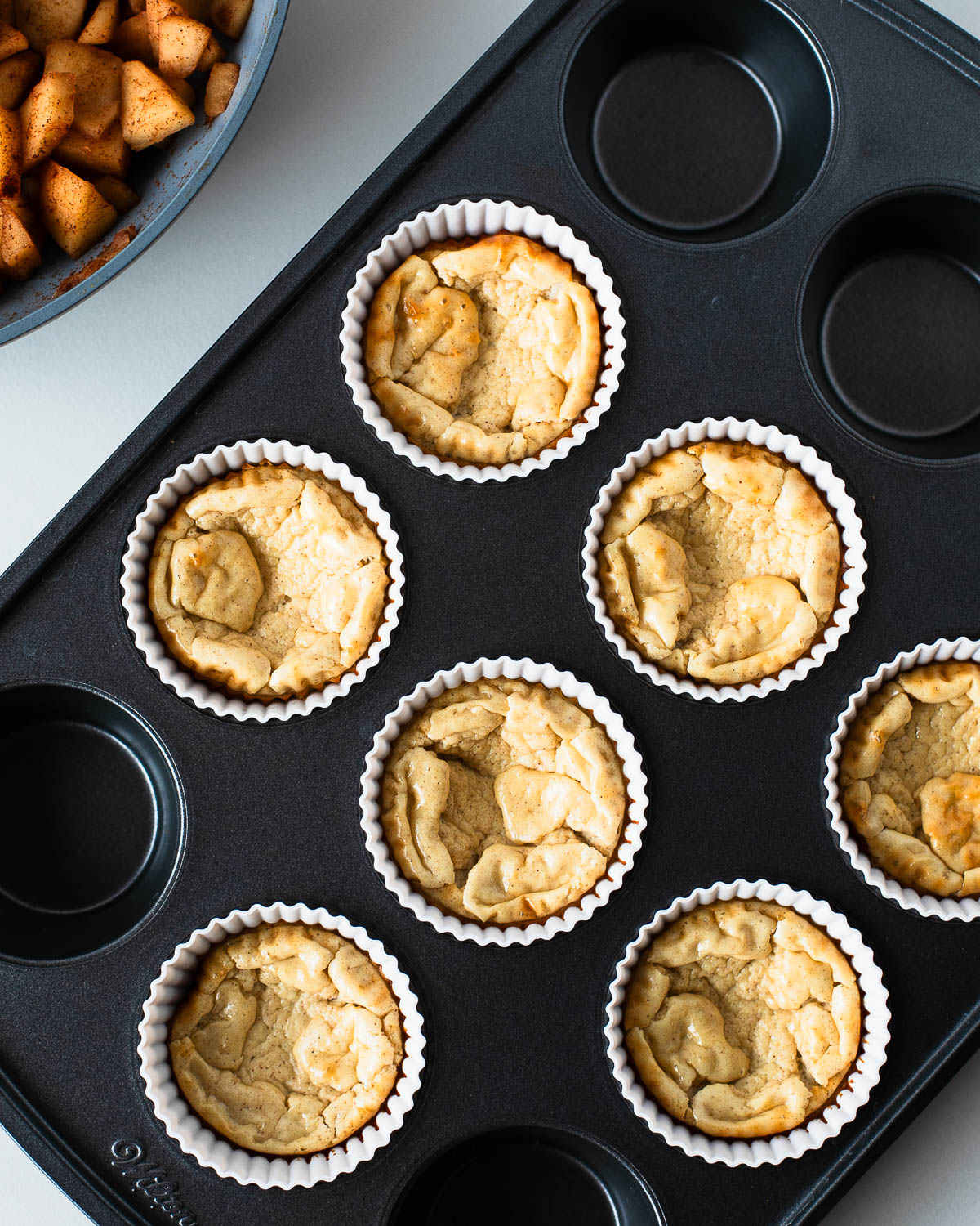 Mini cheesecakes fresh out of the oven, baked golden and cooling in muffin liners.