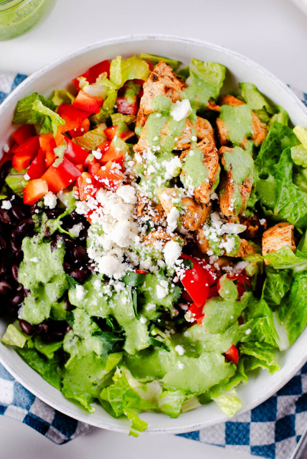 Colorful chicken taco bowl with seasoned chicken, black beans, peppers, lettuce, cotija cheese, and cilantro dressing