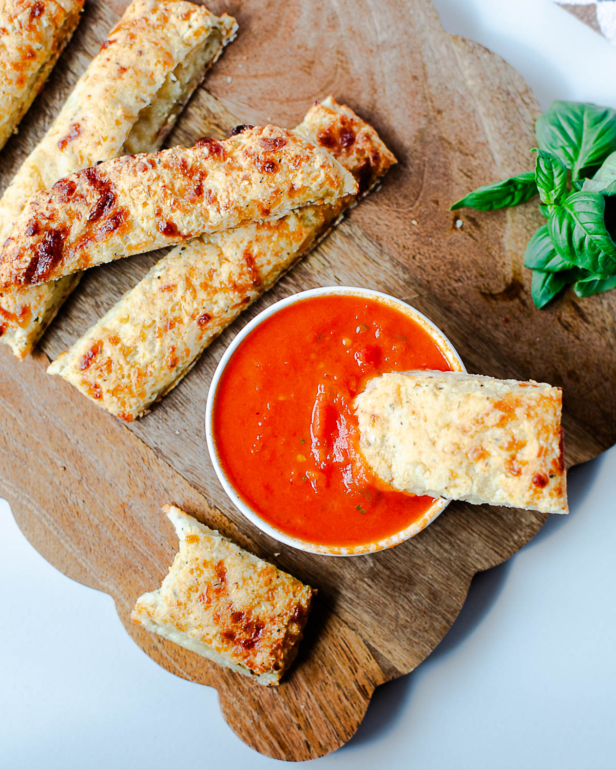 Cottage cheese breadstick dipped into marinara sauce with basil garnish on the side